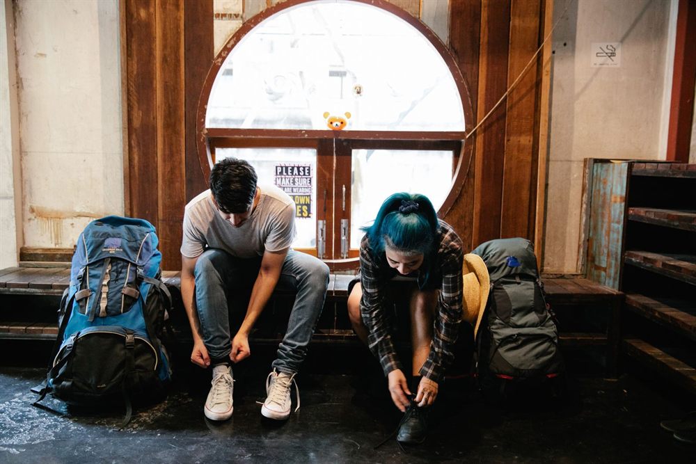 Couple tying their shoes beside packed backpacks, ready to leave