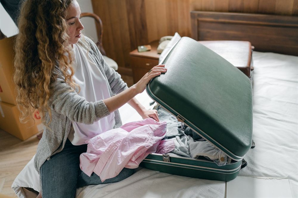 Woman packing clothes into a suitcase on her bed